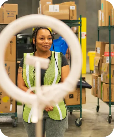 A woman in the Veho warehouse wearing safety jacket, standing in front of a ring light.