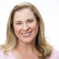 Smiling middle-aged woman with blonde hair wearing a light pink top against a white background.