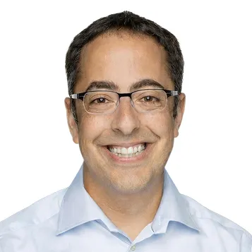 Smiling man with short dark hair and glasses wearing a light blue collared shirt.