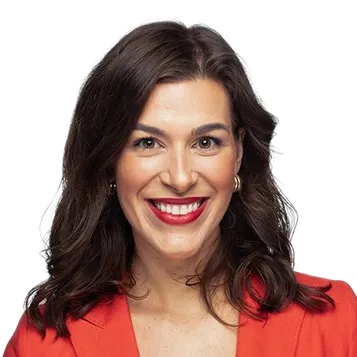 Woman with dark wavy hair wearing a red blazer and smiling against a white background.